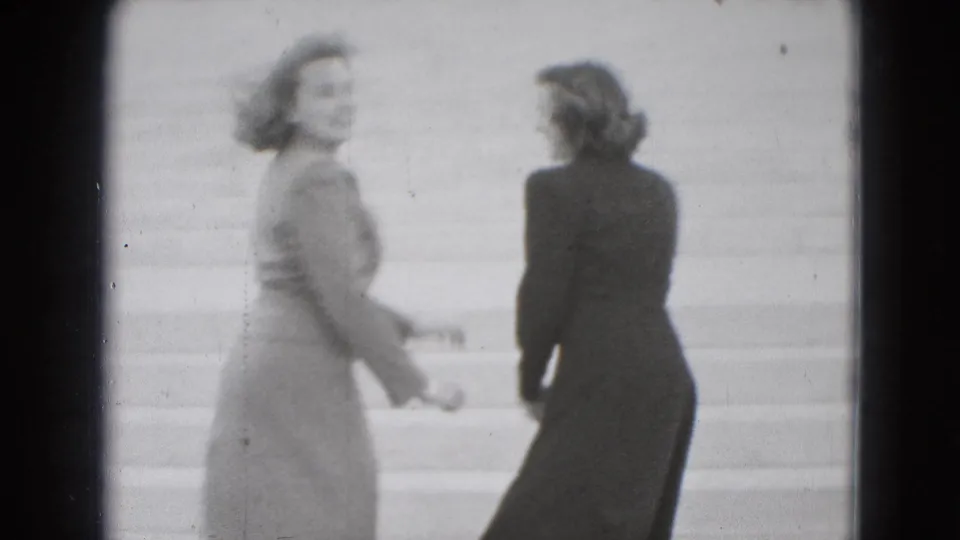 Two young women in 1975 Washington, DC home-movie footage stand playfully on broad stone steps, one looking back toward the camera.