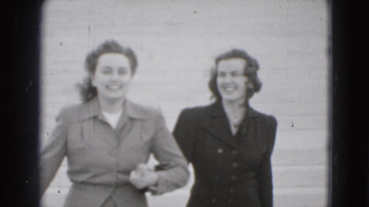 Two young women smile toward the camera while holding hands on broad steps in supplied 1975 Washington, DC footage.