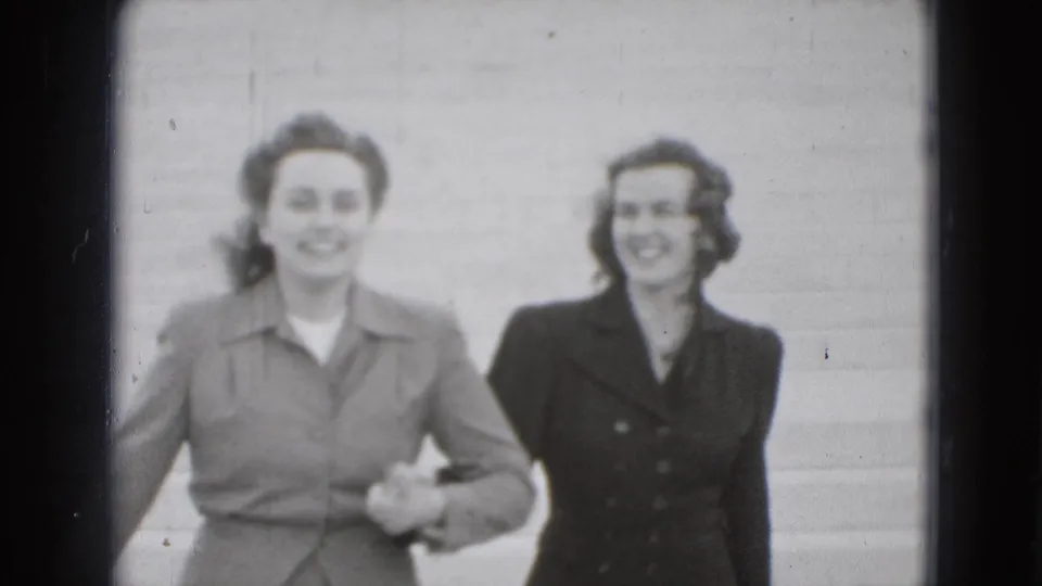 Two young women smile toward the camera while holding hands on broad steps in supplied 1975 Washington, DC footage.