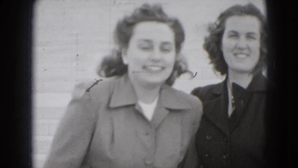 Close, soft-focus 8mm view of two young women smiling beside each other on broad steps in the Washington, DC home-movie clip.