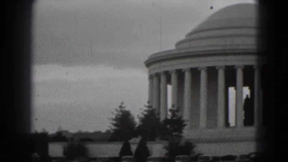 1975 8mm home-movie frame of the Jefferson Memorial in Washington, DC, seen in soft focus under a gray sky with foreground trees.