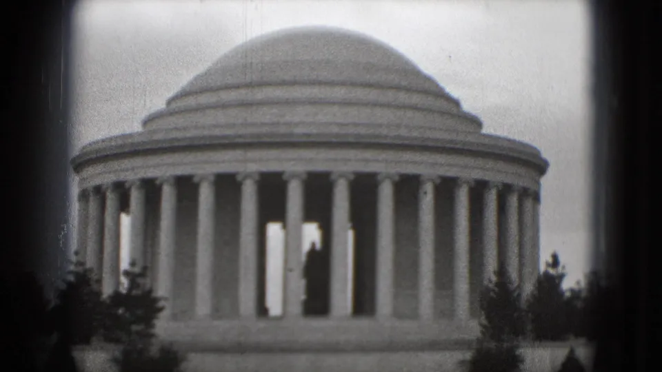 1975 Washington, DC 8mm frame showing the Jefferson Memorial on a gray day, with foreground trees and a distant figure-like silhouette inside.