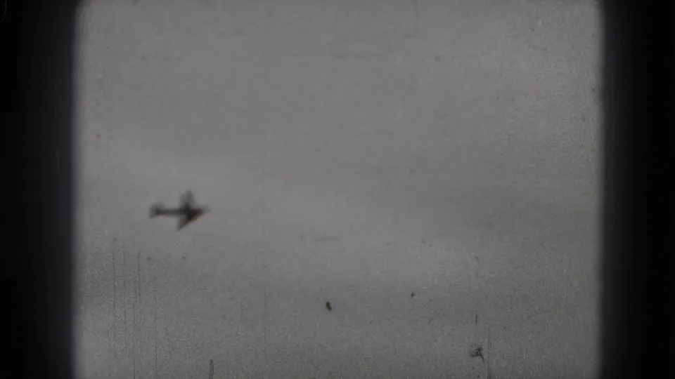 Small airplane silhouette crossing the cloudy Washington, DC sky in a grainy 1975 8mm home-movie frame.
