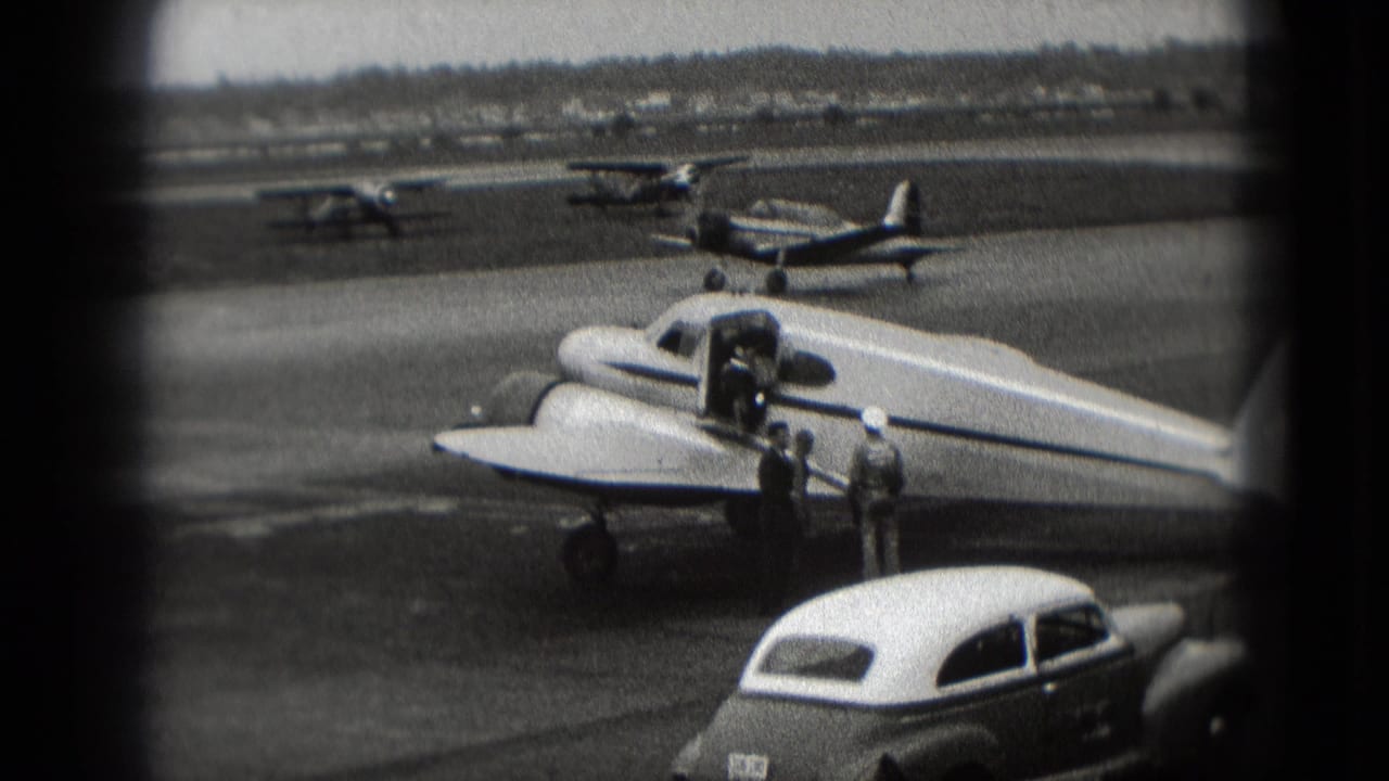 1975 Washington, DC airport home-movie frame showing a small propeller plane, open door, two adults, parked cars, and distant aircraft.