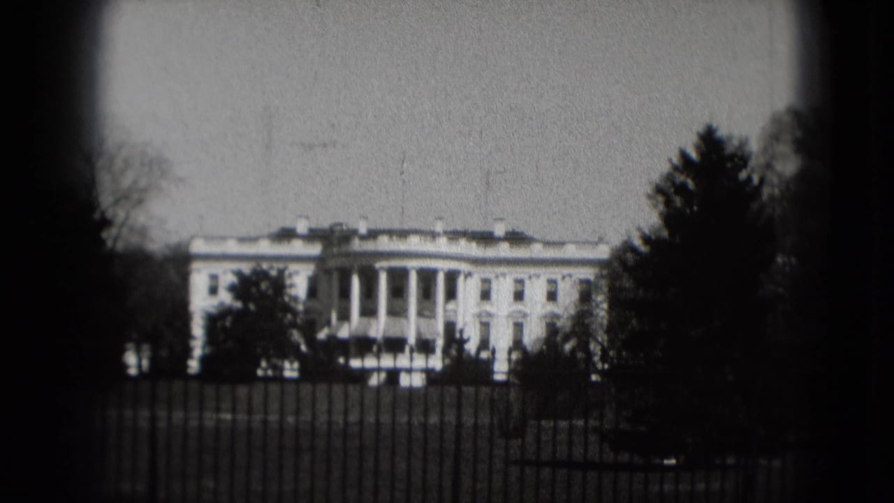 Black-and-white 8mm frame of the White House exterior in Washington, DC, with iron fence, lawn, trees, and soft focus.