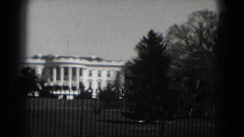 1975 visitor-shot 8mm frame with the White House partly obscured by trees and the iron fence in Washington, DC.