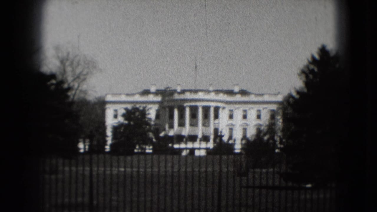 1975 8mm view of the White House in Washington, DC, framed by trees behind an iron fence on a cloudy day.