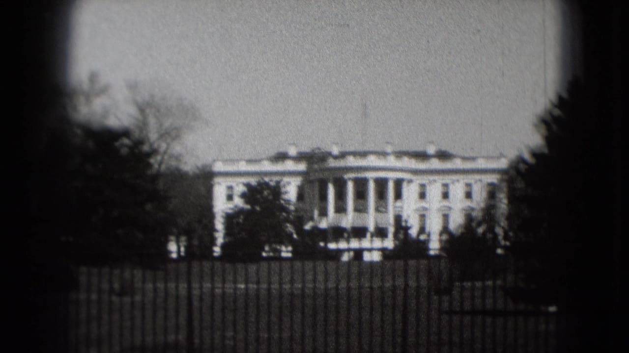 Visitor-shot 1975 view of the White House behind the iron fence, with trees silhouetted against a gray sky.