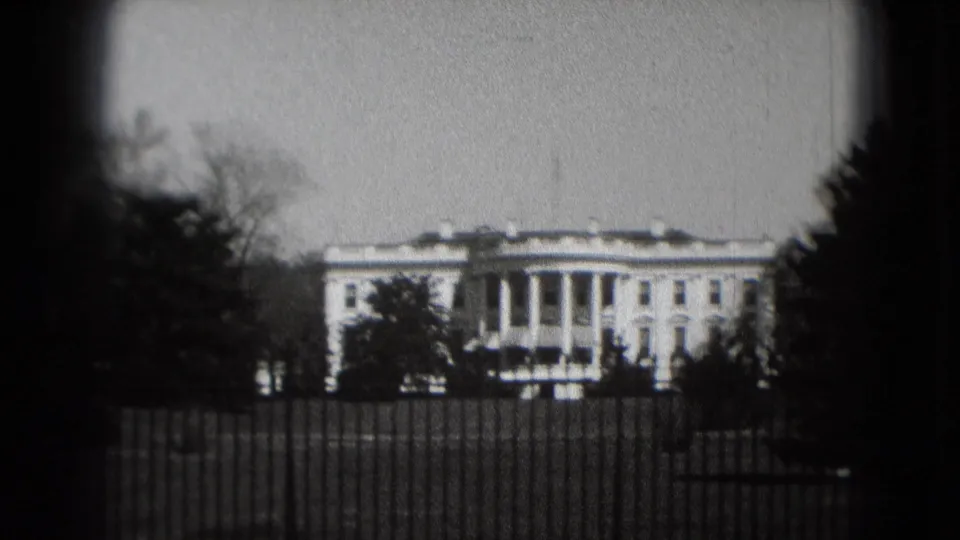 Visitor-shot 1975 view of the White House behind the iron fence, with trees silhouetted against a gray sky.