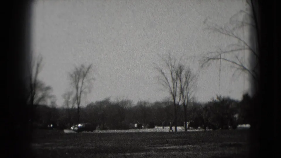 1975 Washington, DC home-movie view across parkland with bare trees, roadway, and distant cars before the memorial appears.