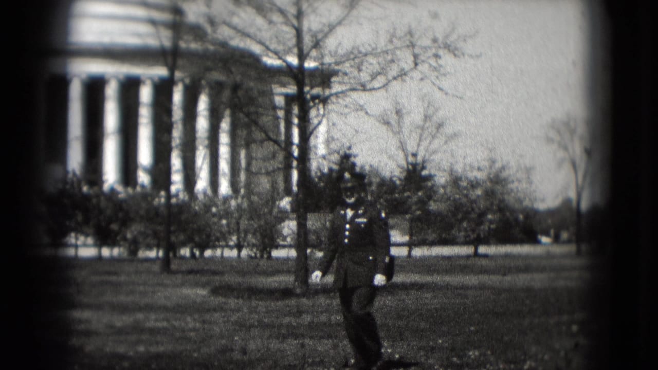A uniformed man walks across the lawn in front of the Lincoln Memorial in Washington DC, seen through grainy 8mm footage.