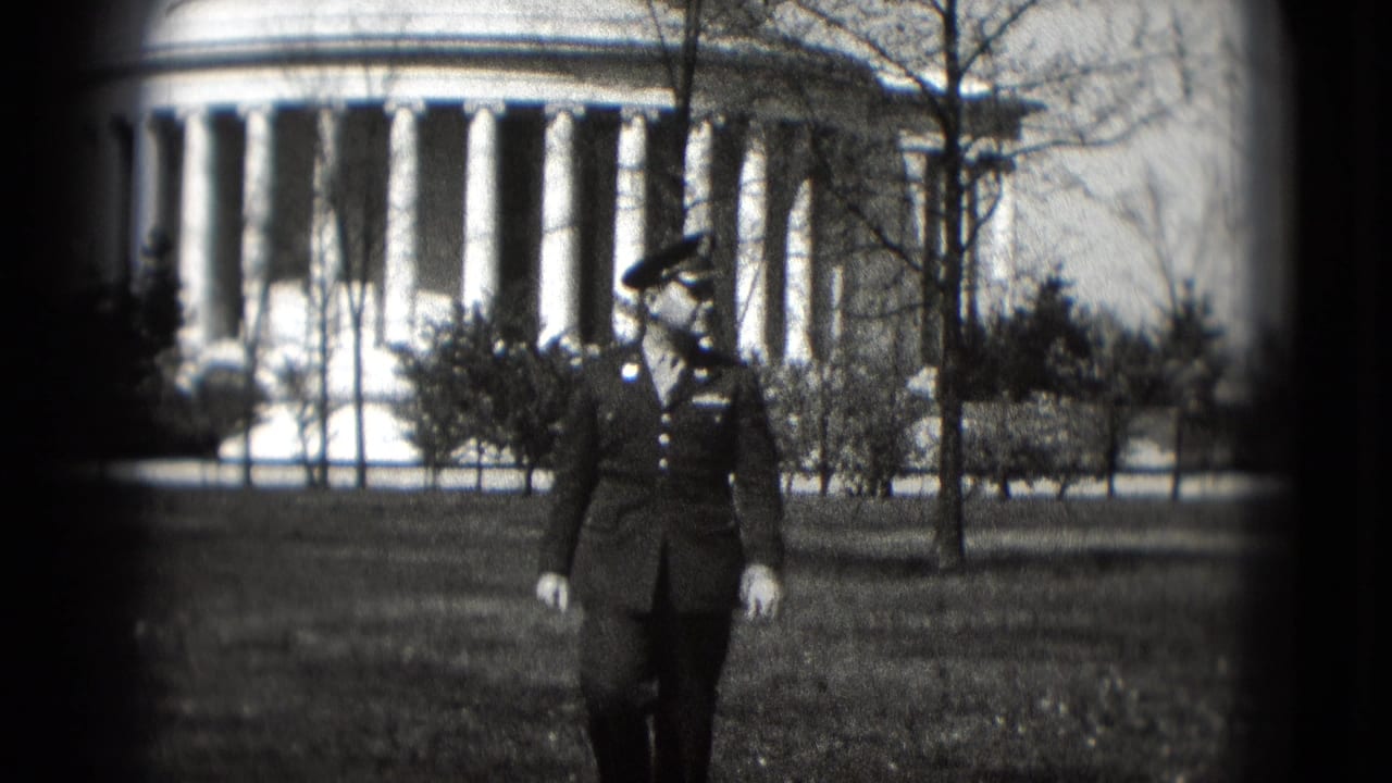 The serviceman remains centered while walking across the grass, with bare trees and a large columned monument visible behind him.