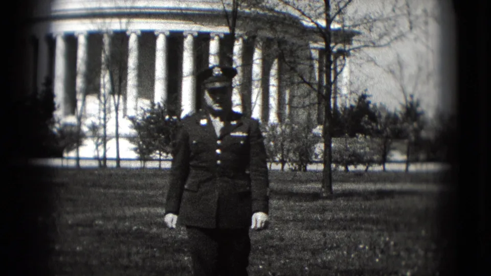 Closer 8mm frame of the uniformed serviceman approaching the camera, with white gloves, dark dress jacket, lawn, and columns visible.