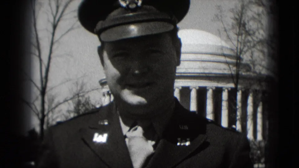 Tight 1975 Washington, DC home-movie frame of a uniformed man, with the Jefferson Memorial dome and columns partly visible in the background.