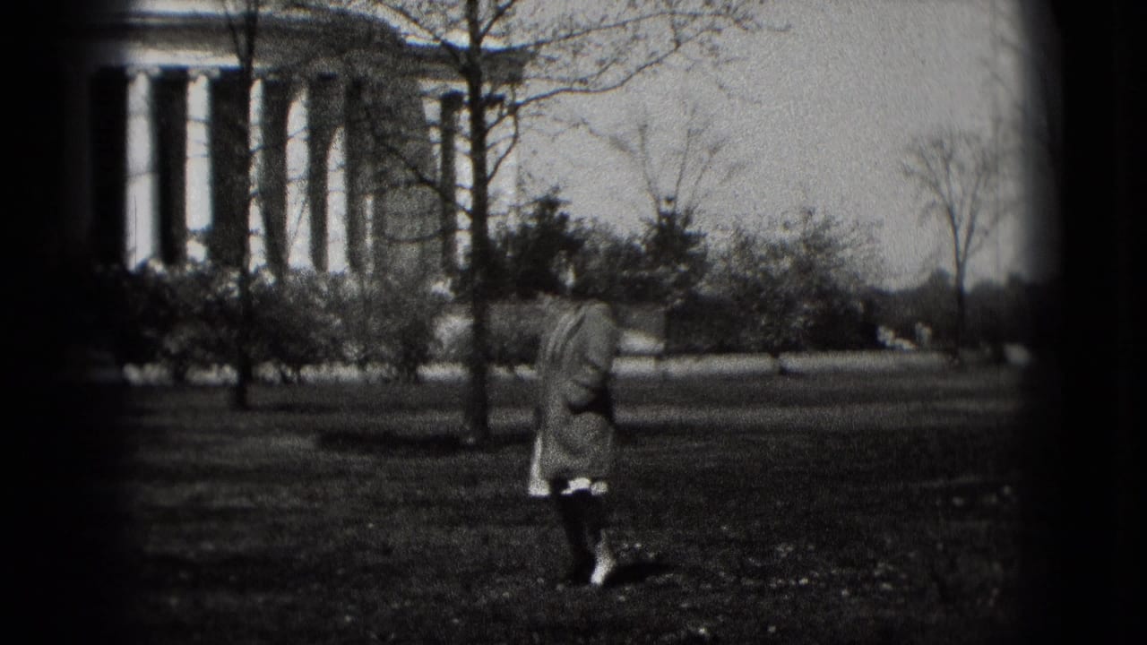 In Washington, D.C., a woman in a long coat walks across a grassy lawn near the Jefferson Memorial in black-and-white 8mm footage.