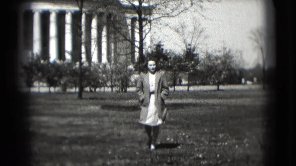 A woman walks toward the camera on grass in front of the Jefferson Memorial, framed by bare trees and soft 8mm exposure.