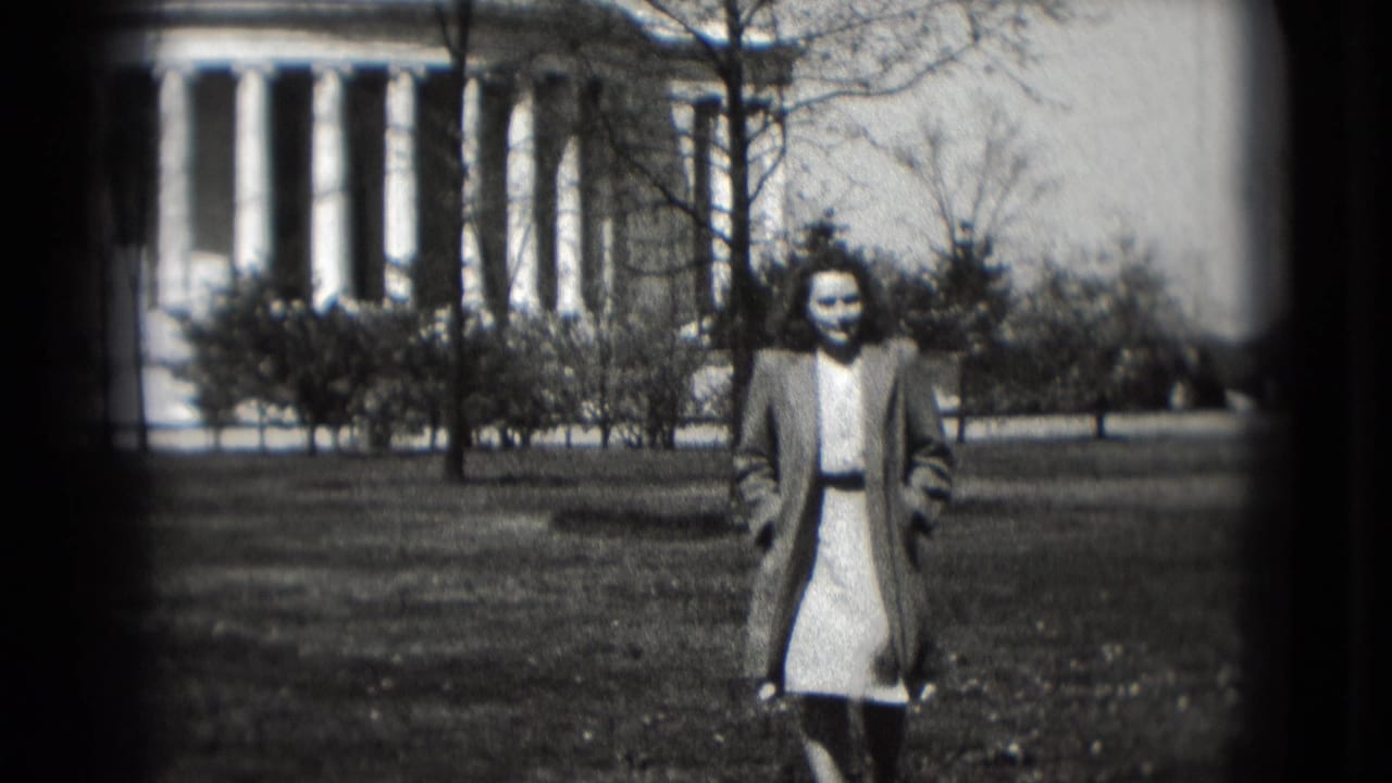 Woman walking on a lawn in front of a white domed columned building.