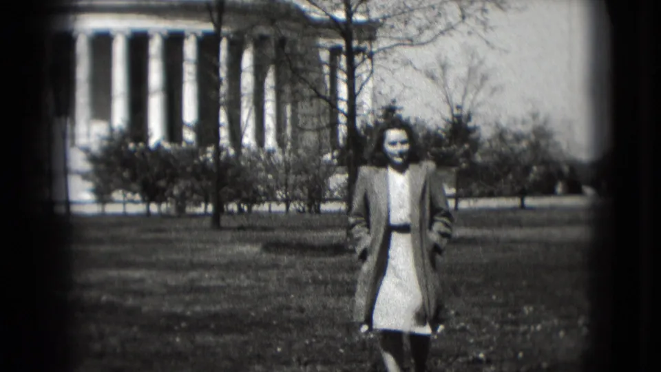 1975 Washington, DC home-movie frame of a woman in a light dress and coat walking across grass before a white domed building.