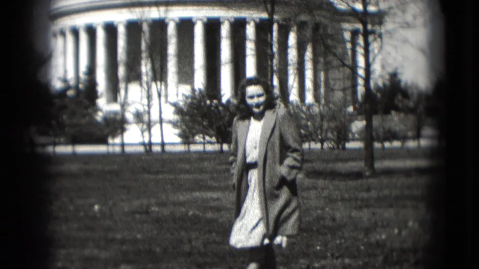 1975 Washington, DC frame showing a smiling woman on grass before a white neoclassical dome and columns.