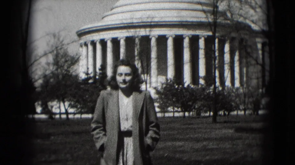 Adult woman in 1970s-style clothing stands on a lawn before the Jefferson Memorial in Washington DC.