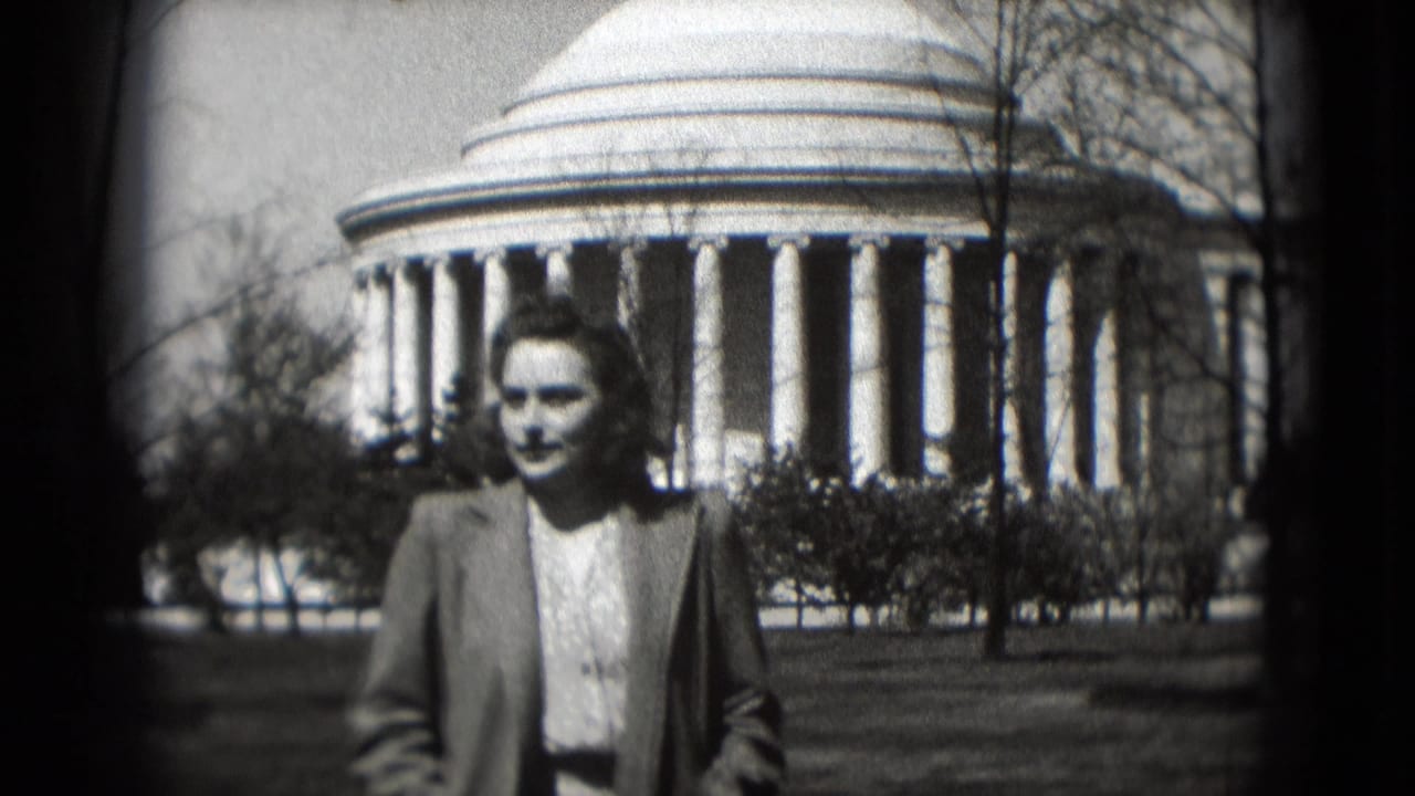Adult woman walks toward the camera in front of the Jefferson Memorial, framed by lawn and bare trees.
