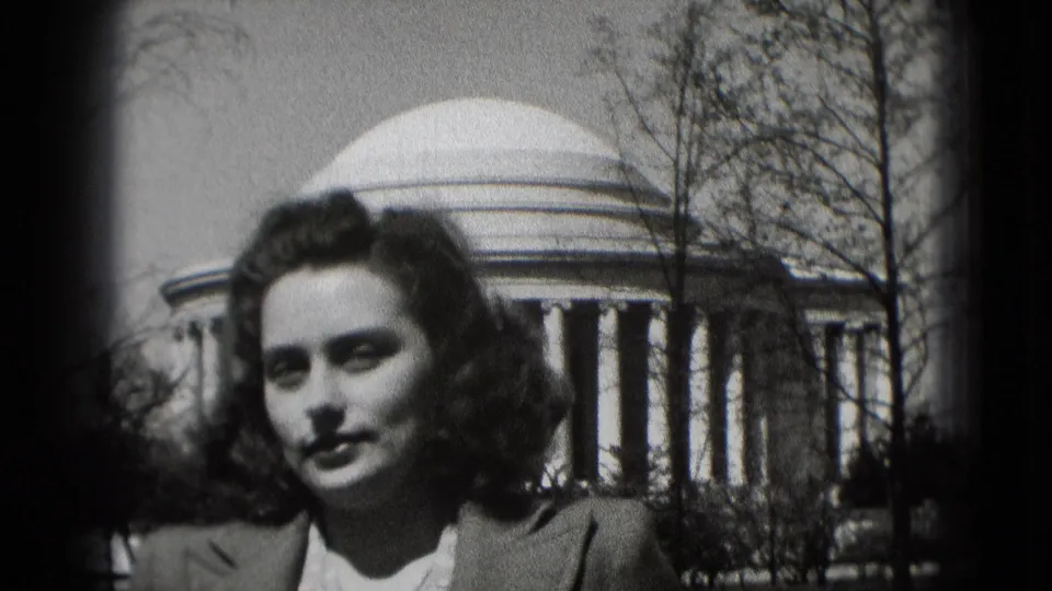 Adult woman faces the camera in a close home-movie view with the Jefferson Memorial visible behind her.
