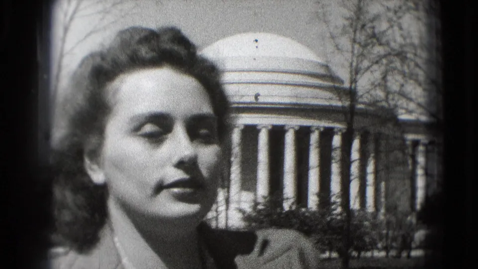 A young woman is filmed from a slightly different angle in Washington, DC, with the Jefferson Memorial dome and columns behind her.