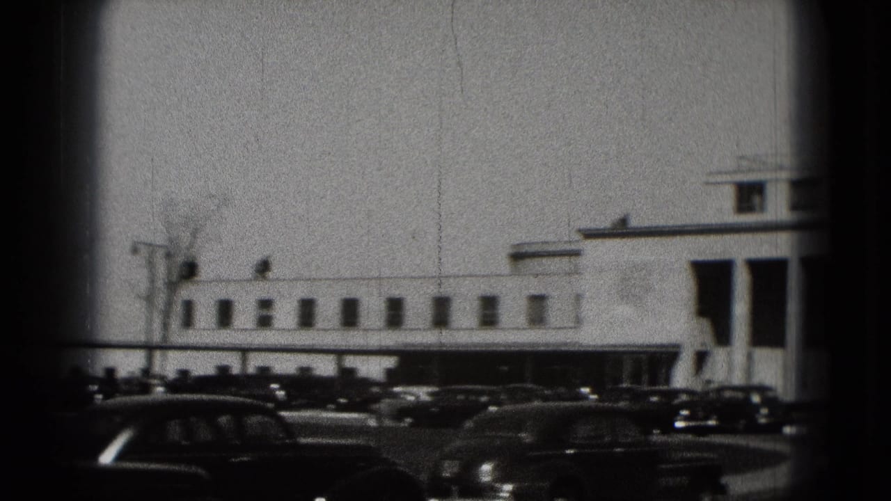 Long white building with parked vintage cars in front.