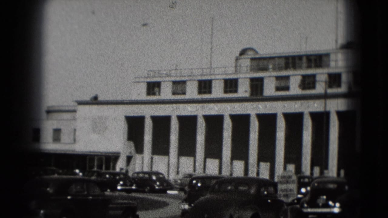 Washington, DC frame showing a white building with tall vertical columns and vintage cars near the curb.