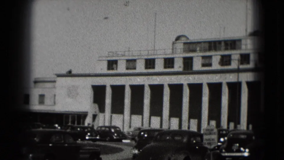 Washington, DC frame showing a white building with tall vertical columns and vintage cars near the curb.
