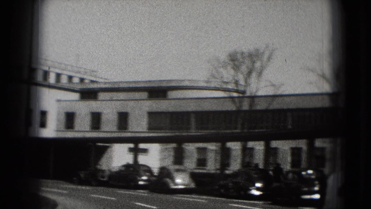 1975 Washington DC 8mm frame showing a white modernist building, curbside older cars, and bare trees through dark film edges.