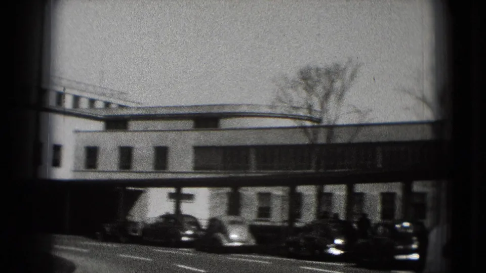 1975 Washington DC 8mm frame showing a white modernist building, curbside older cars, and bare trees through dark film edges.