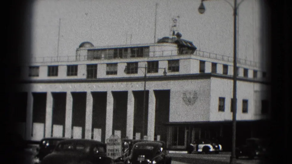 Washington DC airport terminal view on 8mm film, with columned facade, parked older cars, and a vehicle near the entrance.