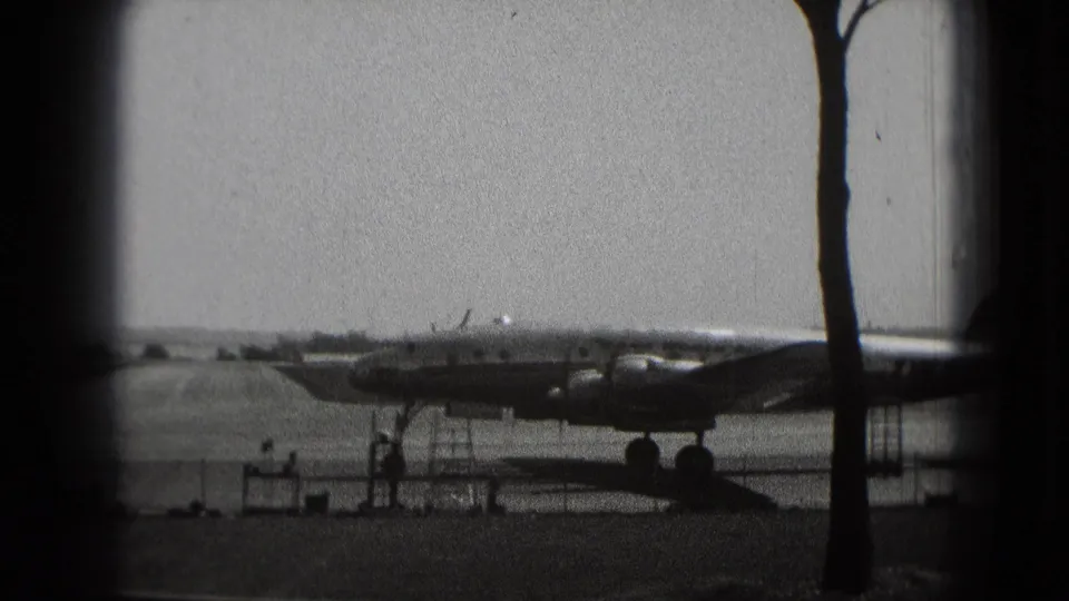 Large passenger airplane on a Washington DC airport tarmac, with ground equipment, trees, sky, and distant people nearby.