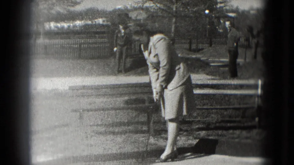 Washington DC 1975 frame of a woman in a light skirt suit and heels preparing to putt near benches and a fence.