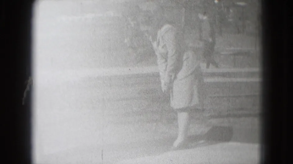 Bright, washed-out 1975 home-movie frame showing the woman mid-putt with bench and outdoor path faintly visible.