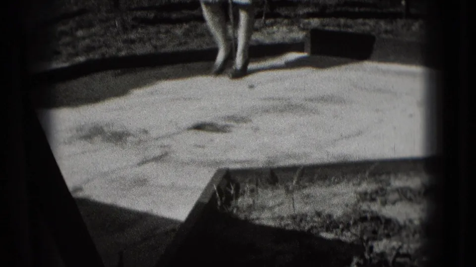 A black-and-white 8mm frame shows the mini-golf surface and ball, with a partly visible adult near the edge of the course.