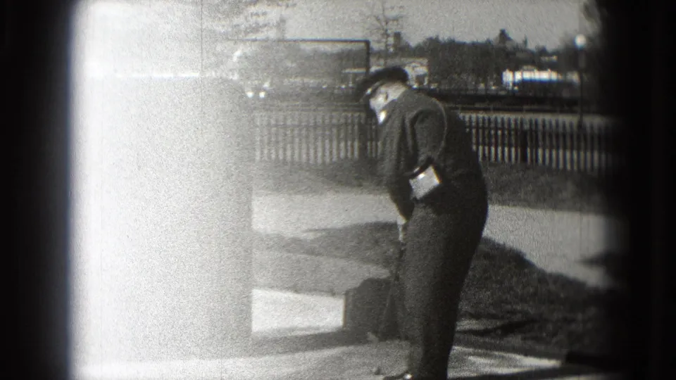 The uniformed man bends toward the mini-golf surface in Washington, DC, with a club and low course feature visible in the grainy 8mm frame.