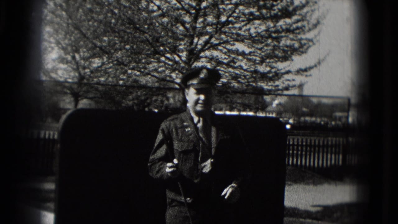 Man in a dark suit and cap stands near a mini golf course outdoors.