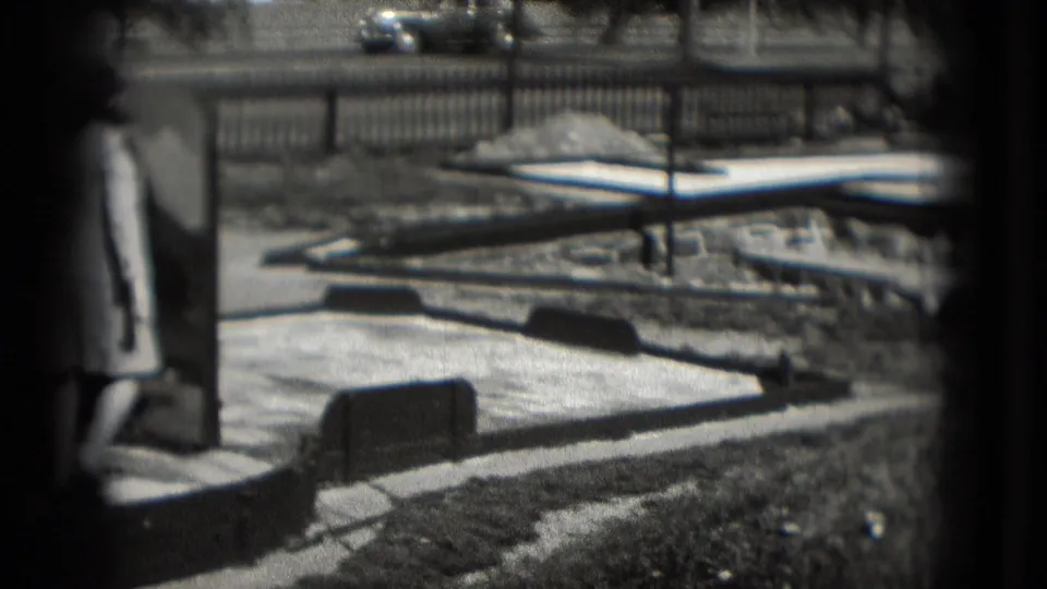 Adult woman stands on the chip-and-putt course in Washington DC, with a picket fence, grass, and roadway visible behind her.