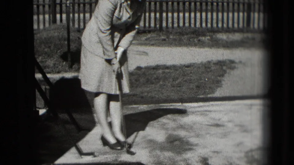 The home-movie frame shows a stylish adult woman leaning into a putting stance outdoors in Washington DC, 1975.