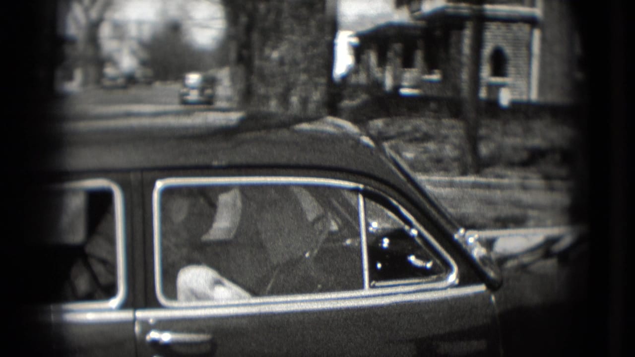 1975 Washington, DC home-movie frame showing a vintage sedan beside houses on a quiet street.