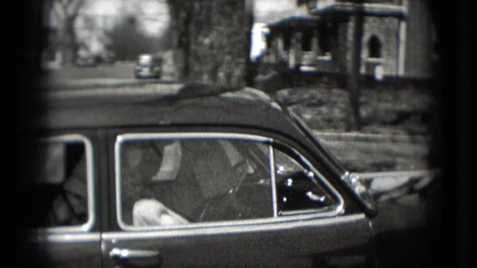 1975 Washington, DC home-movie frame showing a vintage sedan beside houses on a quiet street.