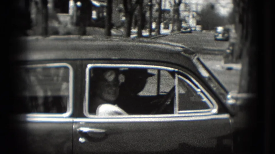 1975 Washington, DC frame showing the driver and passenger inside a vintage sedan during a neighborhood drive.