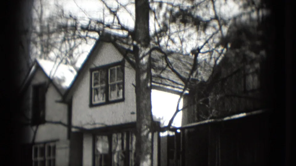 Washington, DC residential houses and bare tree branches appear in a soft black-and-white 1975 8mm home-movie frame.