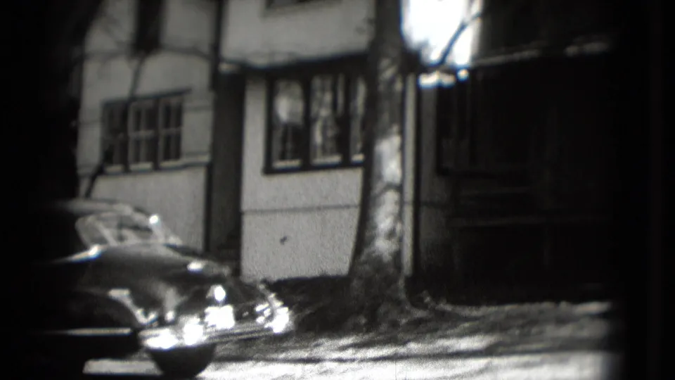 1975 8mm view in Washington DC of a parked mid-century sedan near a two-story residential house framed by bare trees.