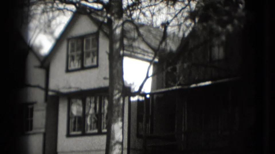 Washington DC residential exterior on 8mm film, showing a two-story house framed by bare trees and a dark railing or fence.