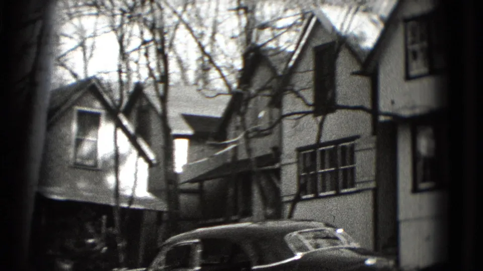 1975 8mm view near Washington, DC, showing detached houses, leafless trees, and part of an older car from a moving vehicle.