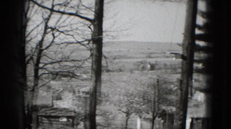Black-and-white 8mm frame with a window or porch post between leafless trees and a distant countryside view near Washington DC.