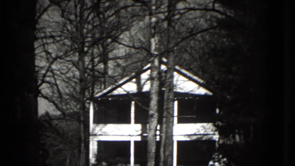 1975 Washington, DC home-movie frame showing a porch-front house partly obscured by leafless trees.